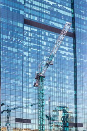 Construction cranes in front of the glass facades of modern office buildingsの写真素材