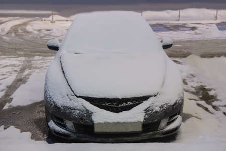 Car in winter in snowfall at evening parkingの写真素材