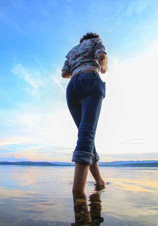 Girl in the water near the lake in the evening at sunsetの写真素材