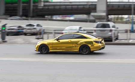 Gold-colored car rides on a city street. Motion blur