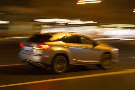 SUV moves quickly through the night city. Motion blur
