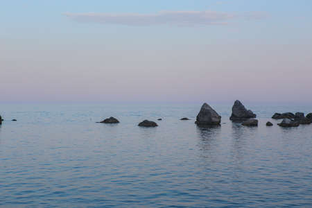 Rocks above the sea surface under a cloudless sky in the evening