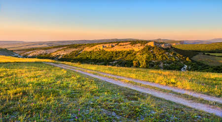 Hilly terrain with ravines and dirt road at sunset.