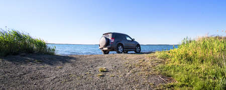 Off-road car on the sandy shore of the lake in the summer at the weekend
