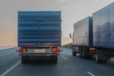 Trucks with trailers move along the highway at sunsetの写真素材