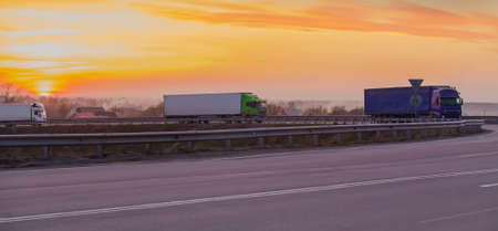 Trucks move at sunset on a suburban highway at a road junction along the villageの写真素材