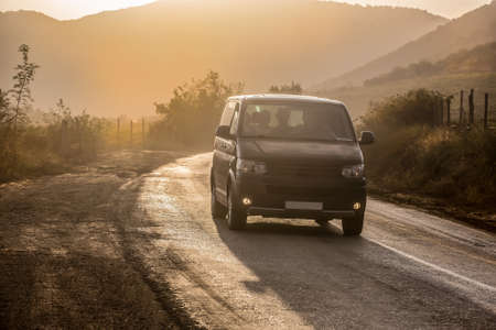 Minibus moves along a winding road in sunlight at sunset