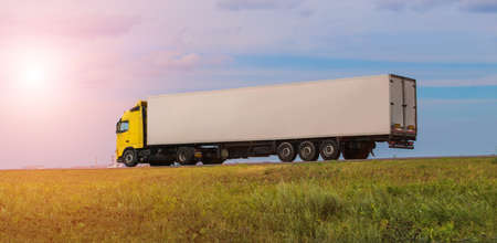 Truck with Container Delivers Cargo on a Country Road against the Background of a Cloudy Skyの写真素材
