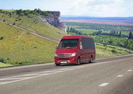 Red minibus moves on a road in the mountains on a summer day