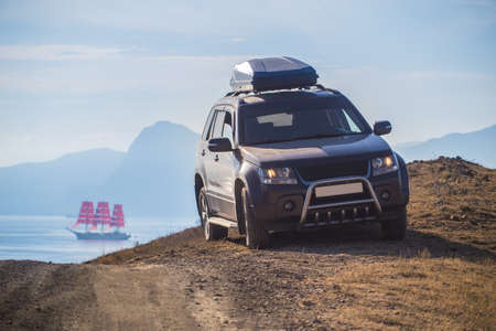 Mountain top SUV and sailboat on the lagoon by the sea