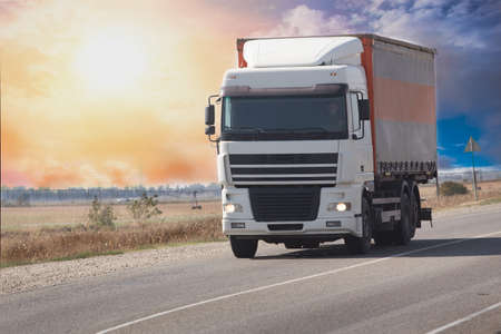 Truck moves on a country road at dawn against the backdrop of a cloudy skyの写真素材