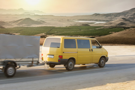 minivan with a trailer drives along the road along a beautiful landscape with mountains and a valley. Blurry motionの写真素材