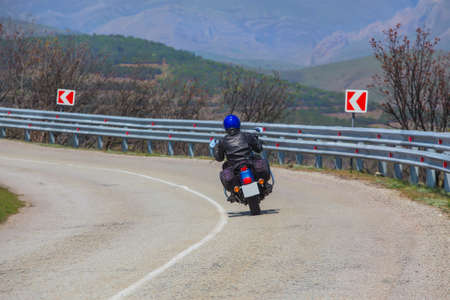 Man on a Motorcycle Turns on a Winding Road against the backdrop of a mountain landscapeの写真素材