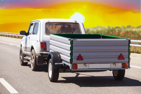 Car with a Trailer Drives on a Suburban Highway at Sunriseの写真素材