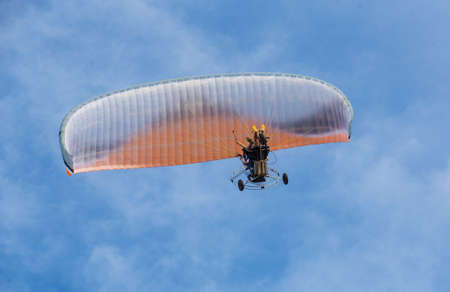 Two men are flying on a motorized paraglider, bottom view.