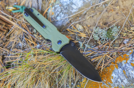 Folding tactical knife on birch roots close-up