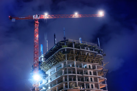 Construction crane near modern high rise building under construction at nightの写真素材