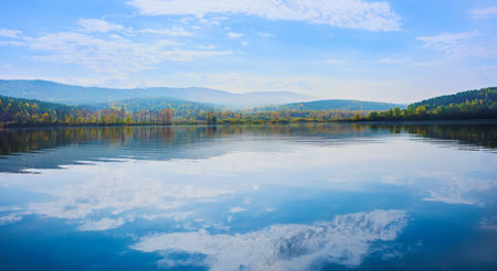 Beautiful Lake surrounded by forests and mountains clouds reflecting on the surface of the waterの写真素材