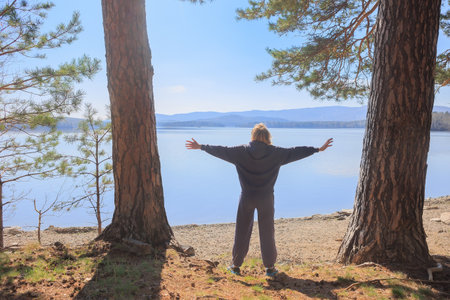 European Girl spread her arms out to the side standing at the edge of a lakeの写真素材