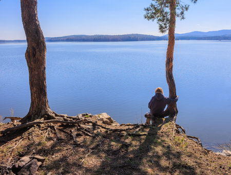 Girl on the high bank of a beautiful lake hugs a tree trunkの写真素材