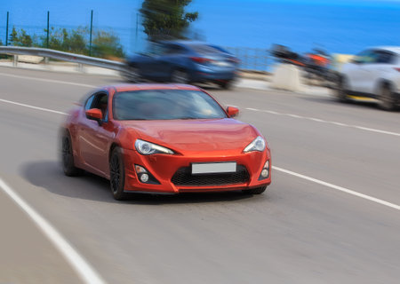 Red sports car rushes along the highway along the coastの写真素材
