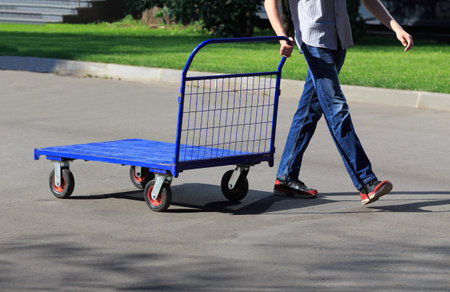 Man pushes a metal cargo cart along the sidewalkの写真素材