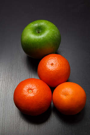 Fresh whole orange tangerines and apple on black tableの写真素材