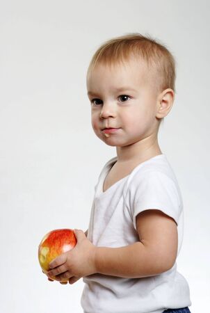 small boy with a red apple on the white grey backgroundの写真素材