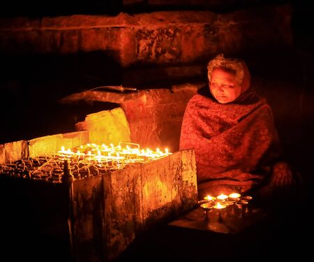 KATHMANDU, NEPAL, APRIL 05: Nepalese elderly woman praying with candles. Kathmandu, Nepal on April 05, 2014のeditorial素材