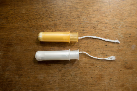 Two tampons with white and orange plastic applicators on wooden tableの写真素材