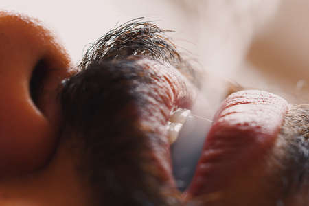 Closeup of a guy with mustache exhaling smoke from mouth