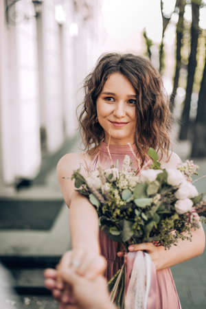 Follow Me! photo with bride in pink dress with a bouquet of the flower. Smiling and happy woman on street. Young bride, bridesmaid. Modern photo style.の写真素材