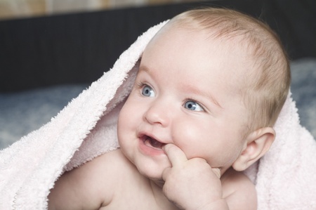 Smiling baby with a towel. Finger in mouth.の写真素材