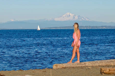 Woman on beach looking at sail boat. Centennial Beach in Boundary Bay Regional Park, Tsawwassen, British Columbia, Canadaの写真素材
