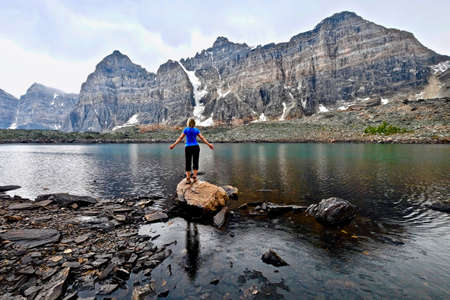 Blond woman by alpine lake enjoying the mountain view on a rainy day. Eiffel lake hike from Moraine lake lodge. Banff National Park. Canadian Rockies. British Columbia. Canada.の写真素材
