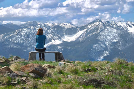 Woman on bench looking at beautiful view of snowcapped mountains of Cascade Range. North Cascades National Park. Winthrop. Washington. United States of Americaの写真素材