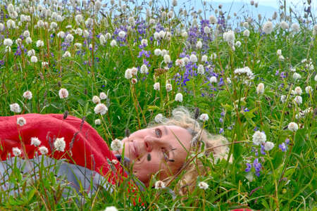 Carefree smiling senior woman lies and relaxes in grass among wildflowers in summer time. Alpine meadows in Pacific Northwest near Seattle. Washington State. United States of Americaの写真素材