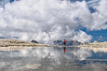Middle age woman hiking in Dolomites Mountains by alpine lake with reflections of peaks and clouds. Summer travel in Italy. South Tyrol. Passo Pordoi. Piz Boe. Italy.の写真素材