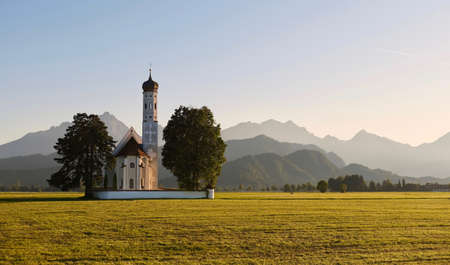 Picturesque landscape in Bavaria. Little old church in green fields with mountain ridge at the background in morning soft light. Bavaria. Germany.の写真素材