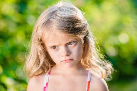 Close-up portrait of capricious blond little girl with pursed lips. Sunny summer day in beautiful...