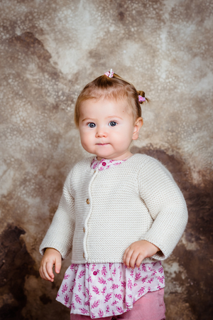 Serious little girl with blond hair and plump cheeks looking at camera. Studio portrait on brown grunge backgroundの写真素材