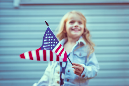 Flying american flag in little girl’s hand. Selective focus, blurred background. Independence Day, Flag Day concept. Vintage and retro colors. Instagram filters Flying american flag in little girl’s hand. Selective focus, blurred background. Independence Day, Flag Day concept. Vintage and retro colors. Instagram filters