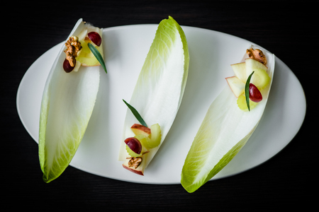 Fancy Waldorf salad on endive leaves served in elegant setting. Waldorf salad on white plate on black table, selective focus on detailsの写真素材