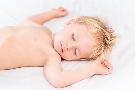 Close-up portrait of little boy with blond hair sleeping on white bad. Carefree childhood conceptの写真素材