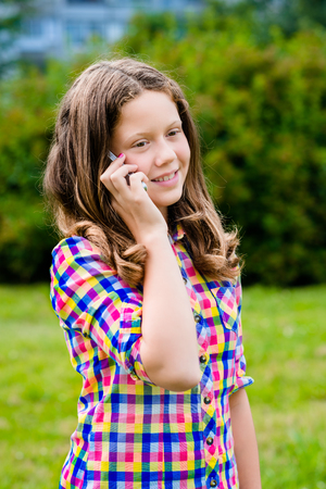Lovely teenage girl in casual clothes speaking by cell phone, in sunny day in summer park. Girl using smartphone. Teenage girl holding smartphone in her handの写真素材