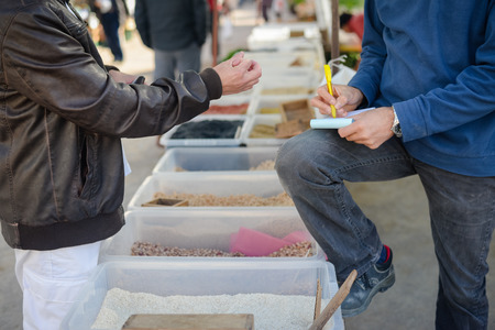 Closeup of businessman hand writing preorder on small notebook standing at market stalls speaking to customerの写真素材