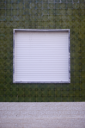 Window with metal roller shutter on the beautiful green wall background outdoorsの写真素材