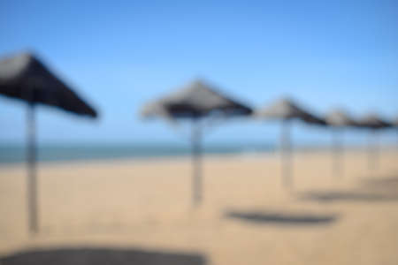 Unfocused silhouettes of exotic beach with palm tree umbrellas, golden sand and blue skyの写真素材