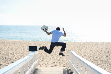 Happy jumping businessman working with computer on the beach background. Back view of flying man...