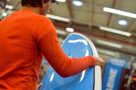 Man choosing and holding a blue surf board on shop or factory background indoorsの写真素材
